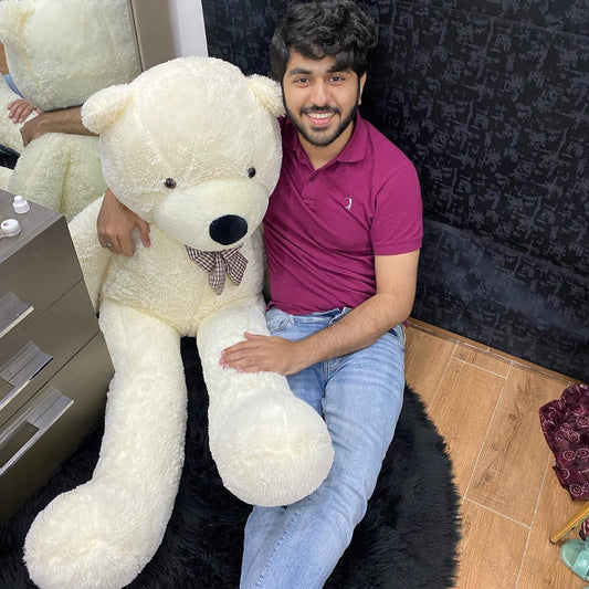 Man sitting on a large black rug with a very large white teddy bear.