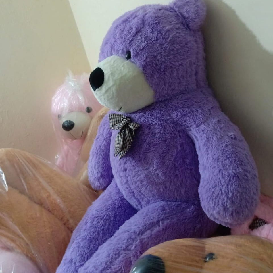 Purple teddy bear with a bow tie sitting on a wooden surface.