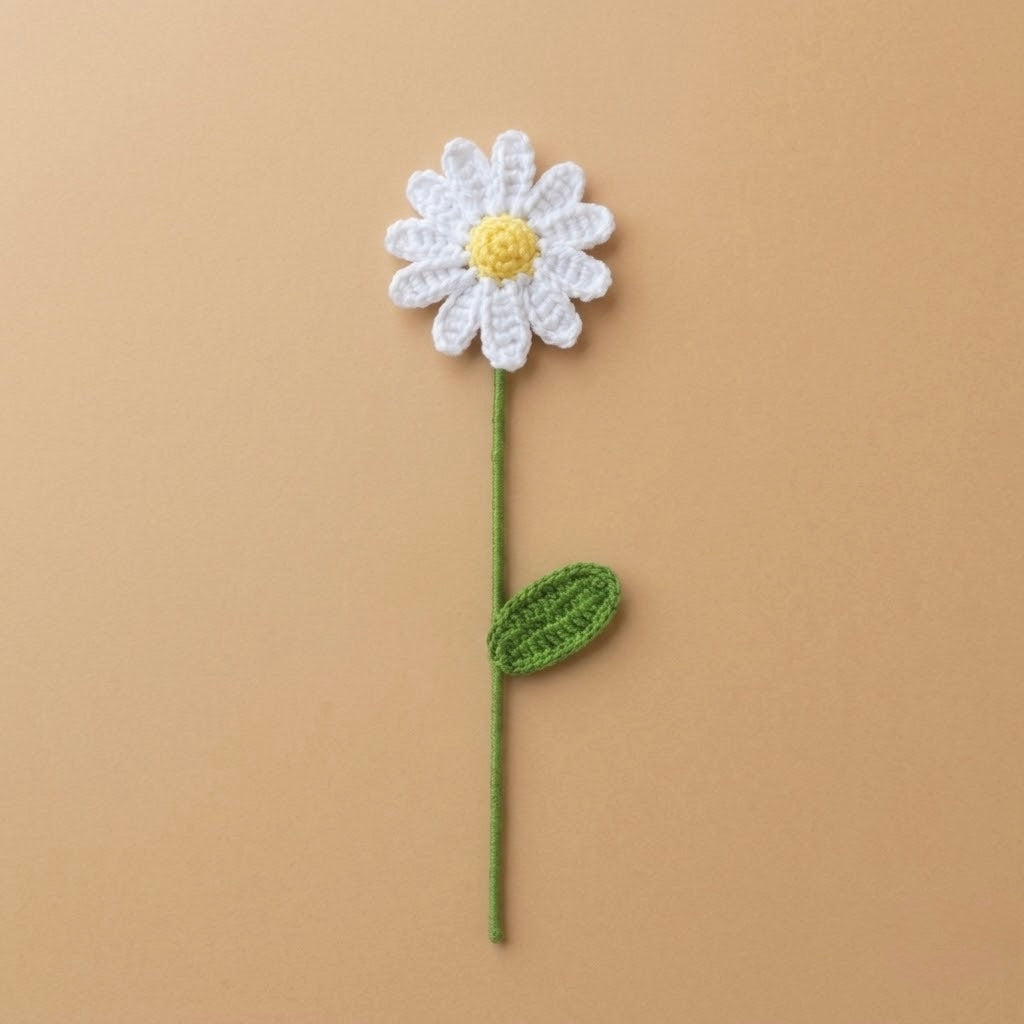 A crocheted daisy flower with white petals, a yellow center, and a green stem and leaf, displayed on a solid tan background.