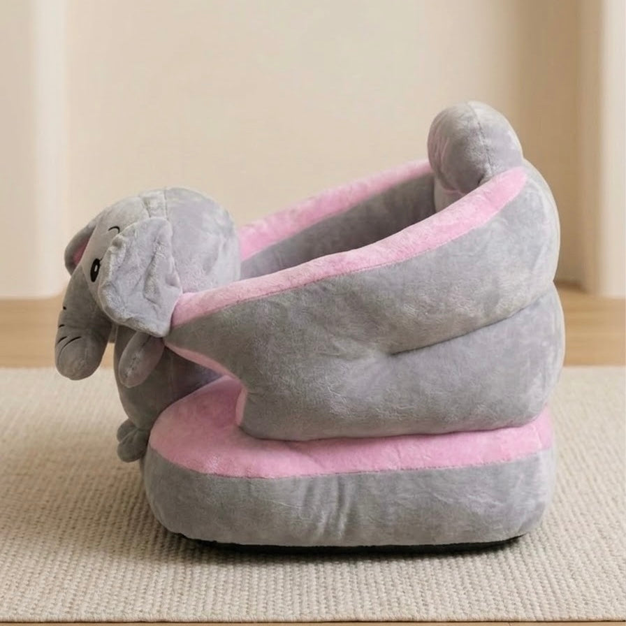 A plush elephant-shaped pet bed in soft gray and light pink, photographed indoors on a woven rug against a neutral beige wall.