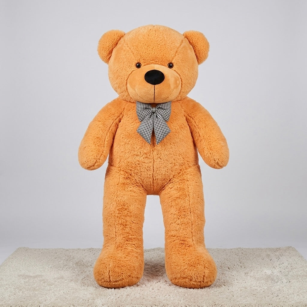 A large plush teddy bear standing upright on a light beige carpet against a plain light gray studio background. The bear is tan/caramel brown with a small black nose, black embroidered eyes, and a gray-and-white checkered bow tie.
