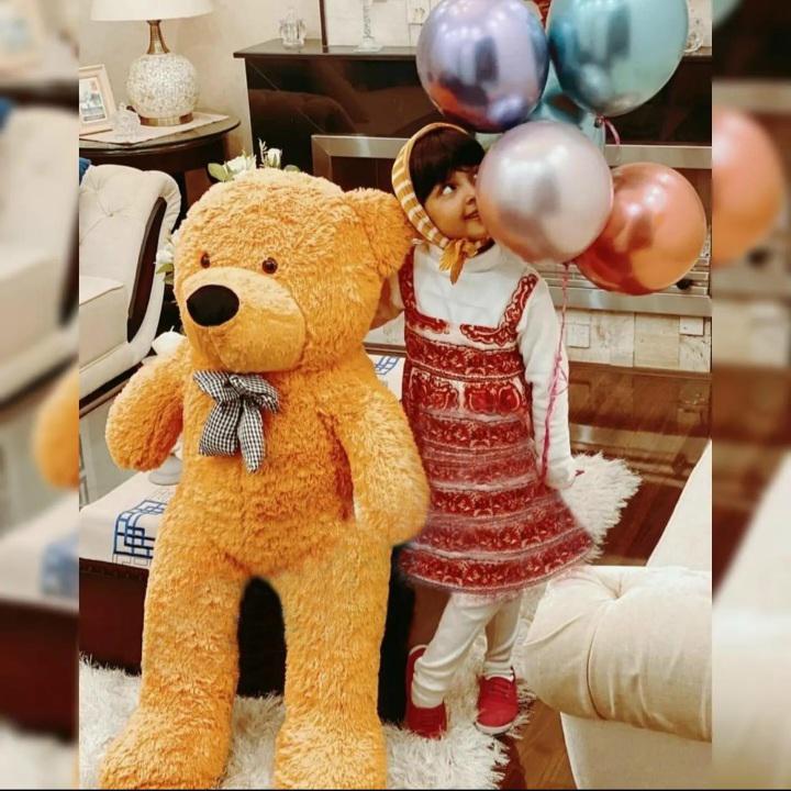 Child holding balloons next to a large teddy bear in a living room setting