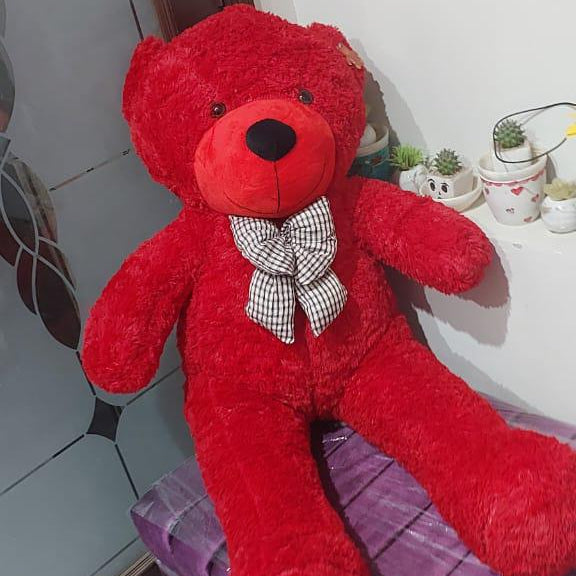 Red teddy bear with a bow tie sitting on a purple surface.