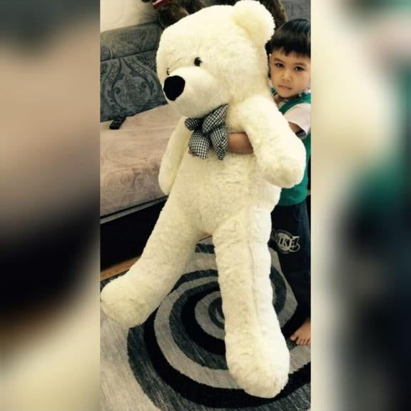 Large white teddy bear held by a child on a patterned rug.