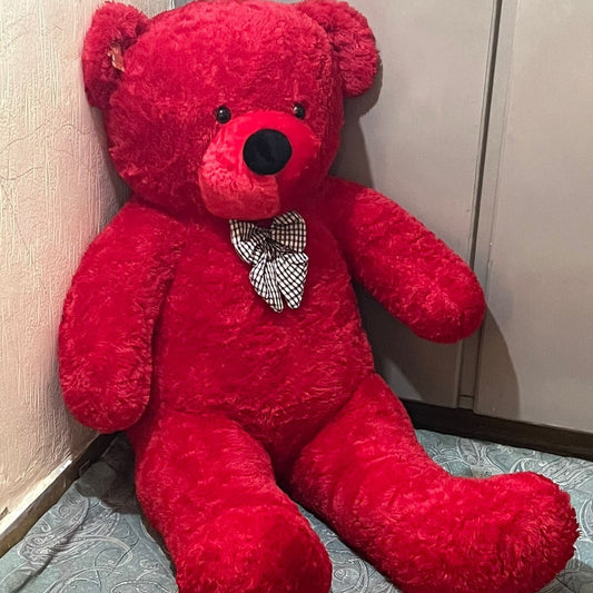 Red teddy bear with a bow tie sitting on a patterned surface.