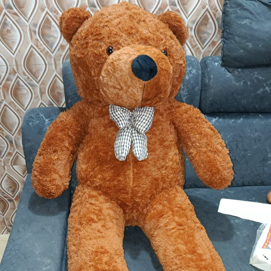 Large brown teddy bear with a bow tie sitting on a dark blue couch.