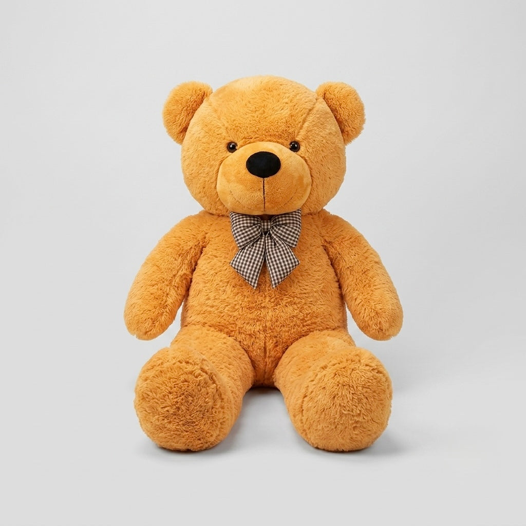 A plush teddy bear in a warm golden-brown color, sitting upright against a light gray studio background. The bear has a small black nose and eyes, and is wearing a small brown and white checkered bow tie.