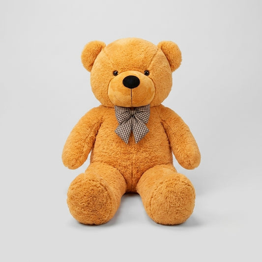 A plush teddy bear in a warm golden-brown color, sitting upright against a light gray studio background. The bear has a small black nose and eyes, and is wearing a small brown and white checkered bow tie.