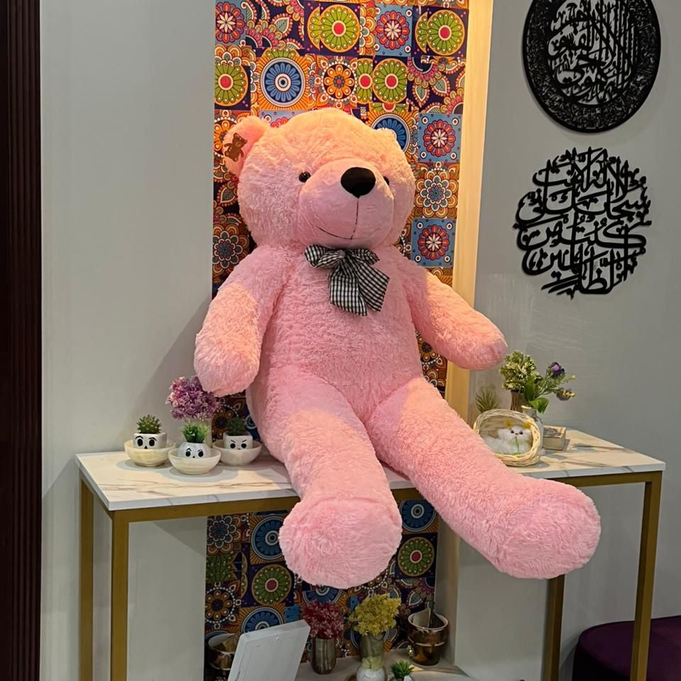 Large pink teddy bear on a marble table with decorative items and colorful wall art in the background.