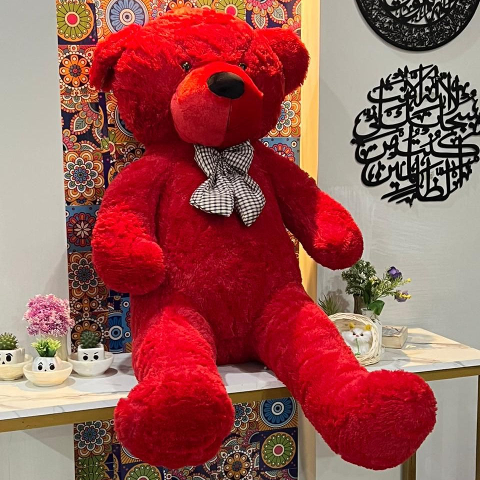 Red teddy bear with a bow tie sitting on a table against a colorful wall.