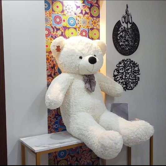 Large white teddy bear sitting on a chair with decorative wall art in the background.