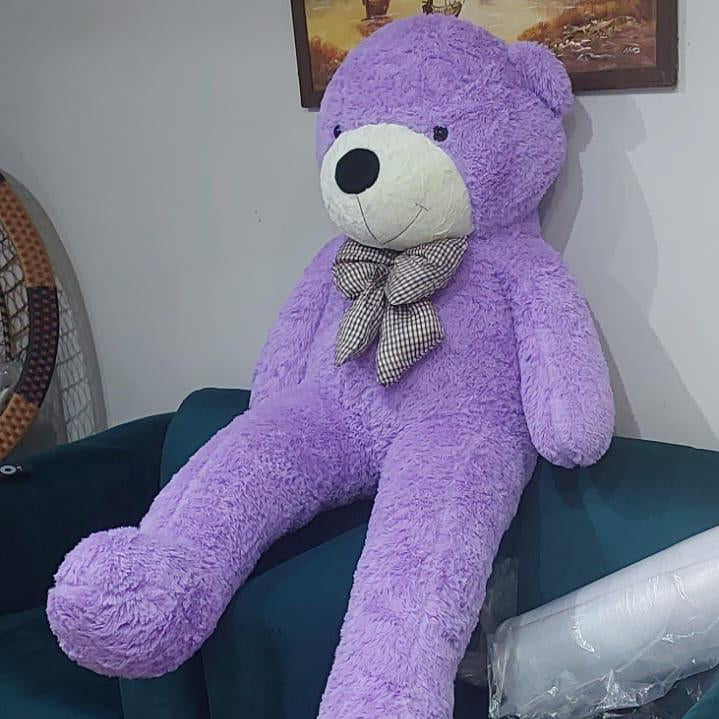 Purple teddy bear with a bow tie on a green surface, with a painting in the background.