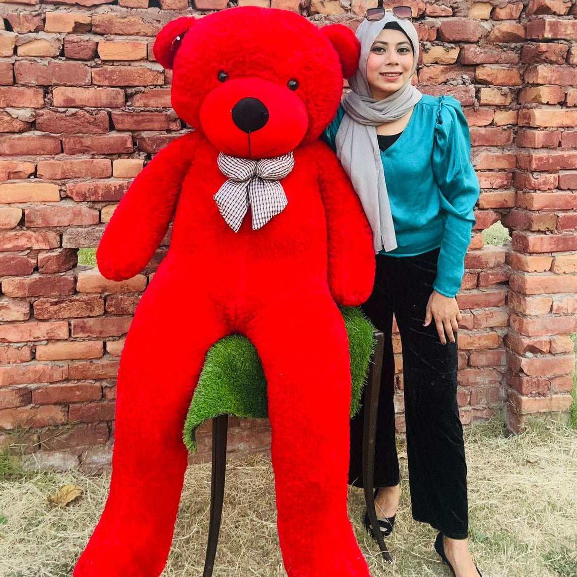 Person holding a large red teddy bear against a brick wall.