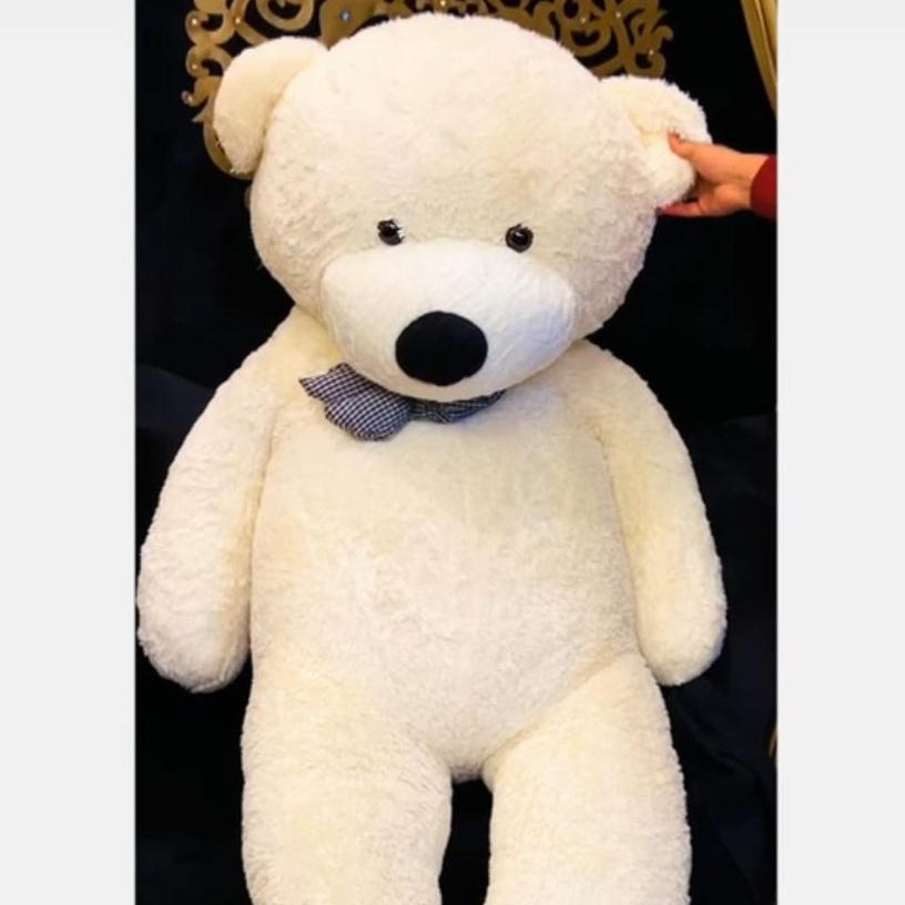 Large white teddy bear with a bow tie on a dark background