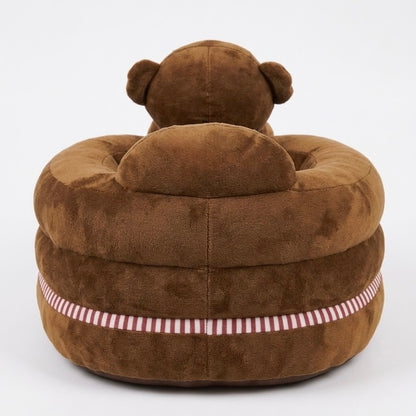 A plush brown teddy bear chair with a circular cushioned base and a small bear head on top, featuring a red and white striped band around the lower side, shown against a plain white background.