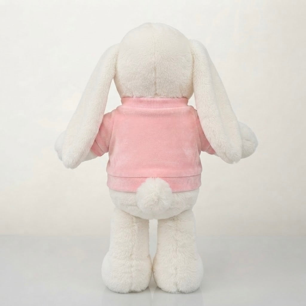A white plush bunny toy viewed from the back, wearing a pink short-sleeve shirt with a small fluffy pom-pom on the back, set against a plain light background.