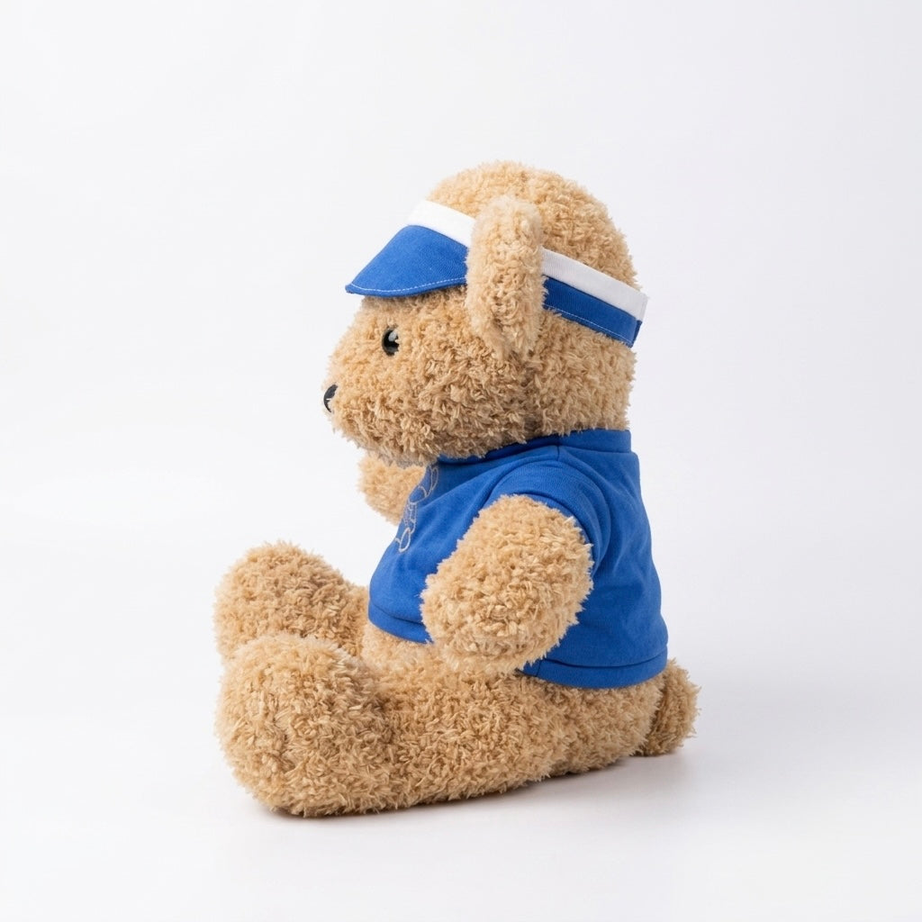 A plush teddy bear toy in light brown fur, wearing a blue visor with a white stripe and a matching blue shirt, sitting against a plain white studio background.
