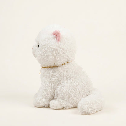 A white fluffy plush kitten toy sitting in profile on a warm off-white background, with a small pink inner ear and a thin gold collar.