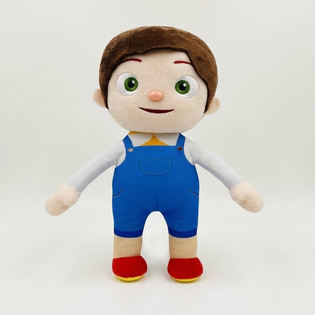A plush toy doll with brown hair, a beige face, green eyes, wearing blue overalls, a white shirt, and red shoes, standing against a plain light gray background.