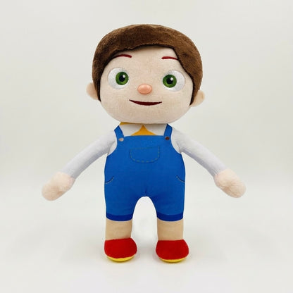 A plush toy doll with brown hair, a beige face, green eyes, wearing blue overalls, a white shirt, and red shoes, standing against a plain light gray background.