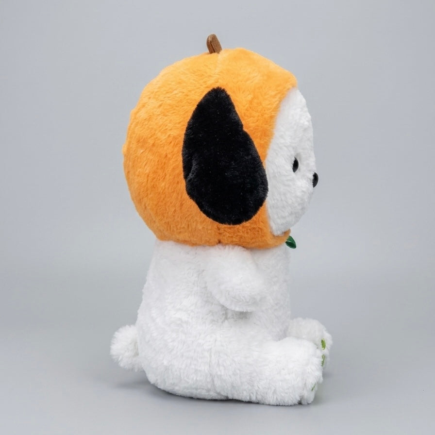 A plush dog toy sitting on a light gray studio background, wearing a bright orange pumpkin-shaped hood with a black ear and small brown stem.