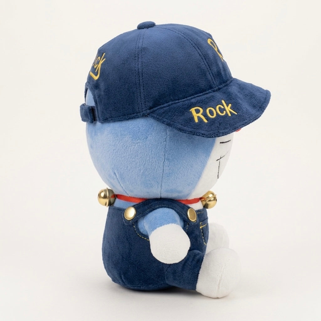 A blue plush character doll wearing a navy blue baseball cap with yellow embroidered text, blue overalls, a red collar with gold bells, and white gloves, photographed on a clean white background.