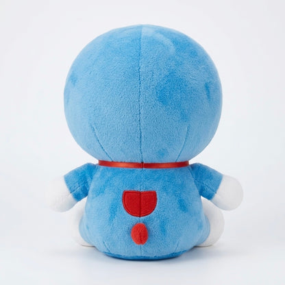 A blue plush toy shown from the back, featuring a round head, white hands and feet, a red collar, and red back details, photographed against a clean white background.