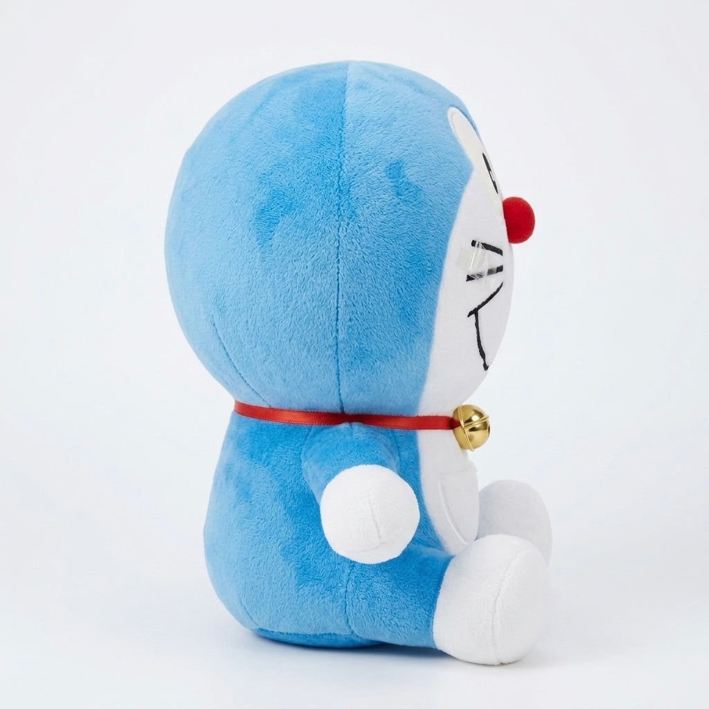 A blue and white plush toy resembling Doraemon, shown from the back and side against a clean white background. The plush has a red nose, a red collar with a small gold bell, and white feet and face details.