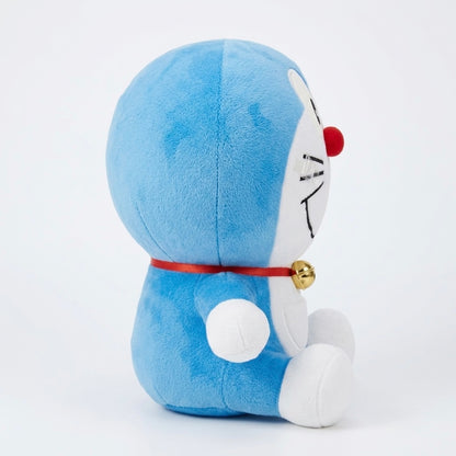 A blue and white plush toy resembling Doraemon, shown from the back and side against a clean white background. The plush has a red nose, a red collar with a small gold bell, and white feet and face details.