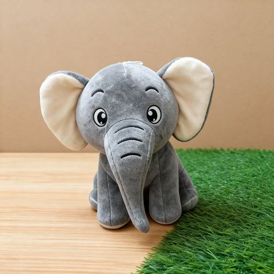 Plush elephant toy on a wooden surface with a grassy area in the background