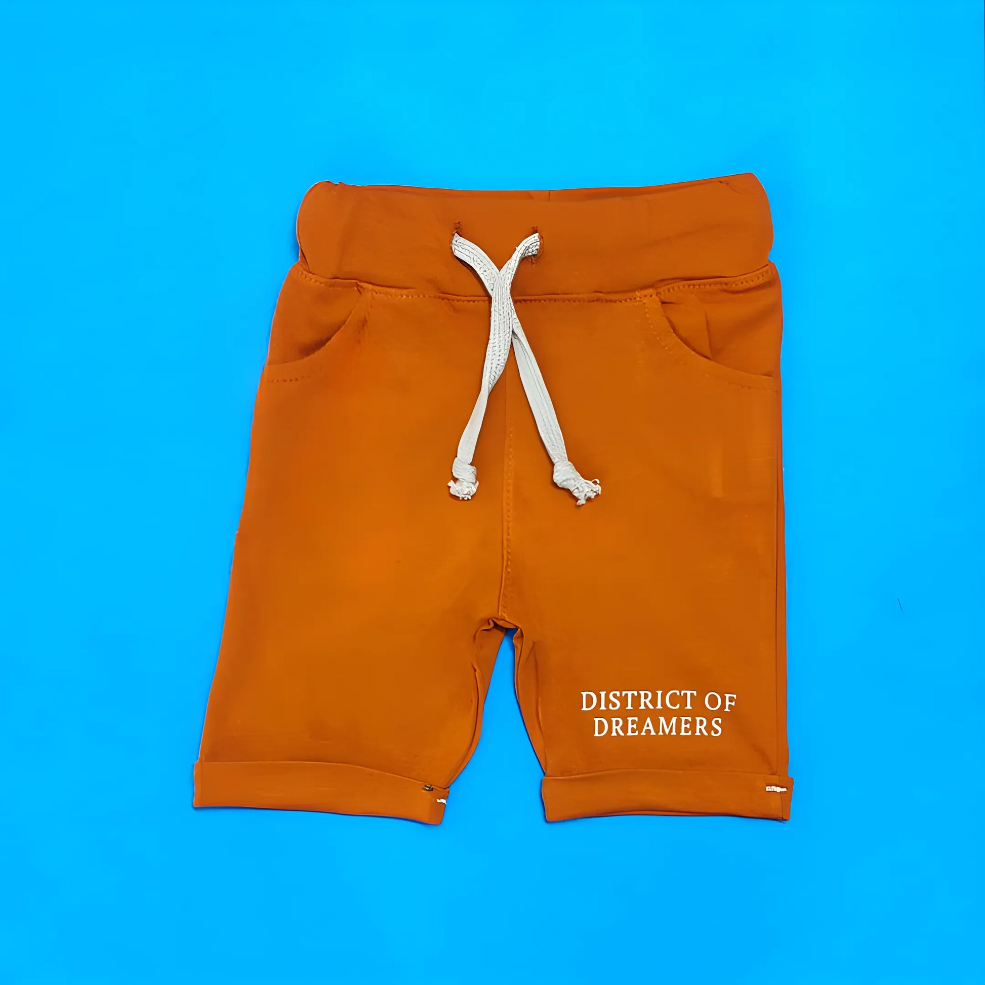 Orange shorts with a white drawstring on a blue background, featuring 'District of Dreamers' text.
