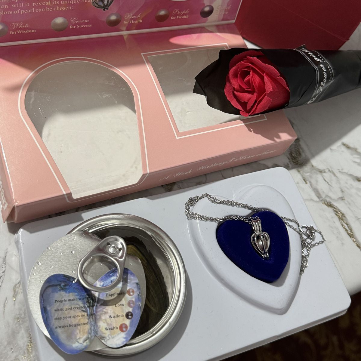 Jewelry set with heart-shaped box, necklace, and red rose on marble surface