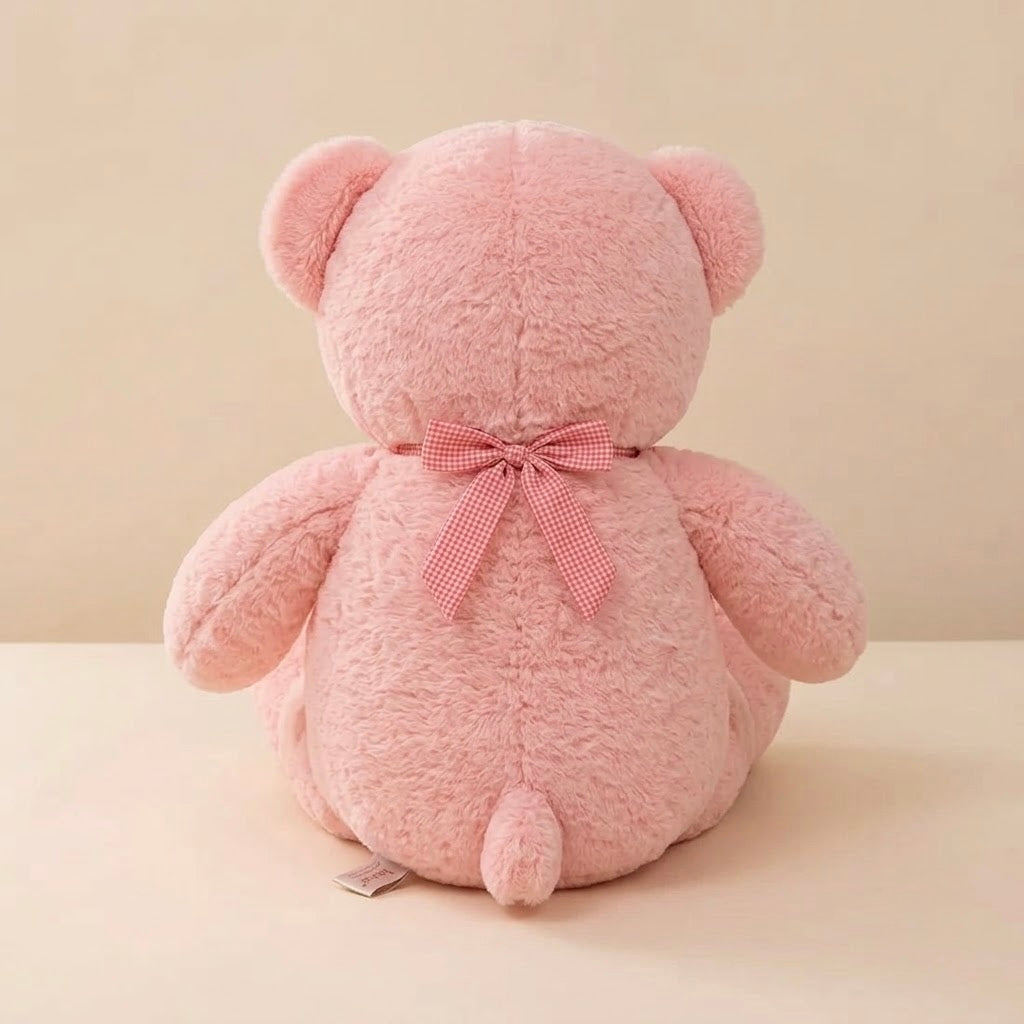 A pink plush teddy bear viewed from the back, featuring soft textured fur and a matching pink gingham bow tied around its neck, set against a warm beige background.