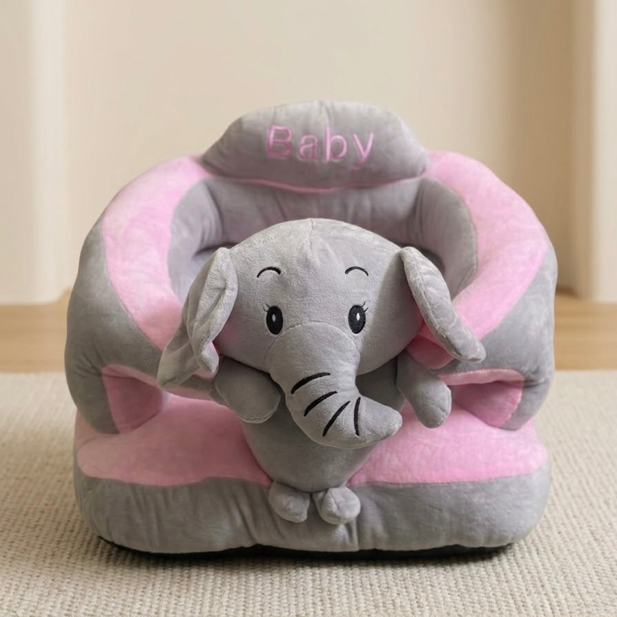 A plush baby elephant toy sitting inside a pink and gray cushioned pet chair with the word 'Baby' embroidered on the headrest, placed on a beige textured rug.