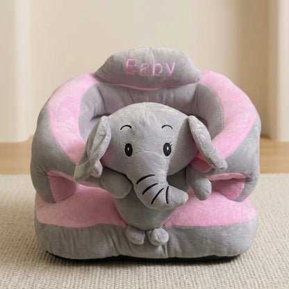 A plush baby elephant toy sitting inside a pink and gray cushioned pet chair with the word 'Baby' embroidered on the headrest, placed on a beige textured rug.