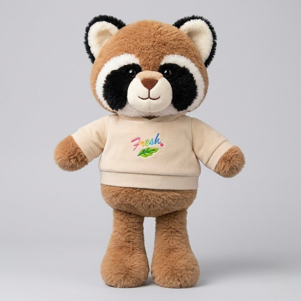 A plush raccoon toy wearing a beige hoodie with a colorful 'Fresh!' graphic, standing against a light gray studio background.