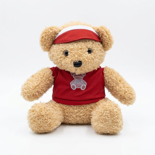 A plush teddy bear wearing a red shirt with a small gray bear graphic and a red visor with a white stripe, photographed against a clean white background.