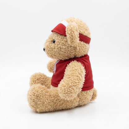 A plush teddy bear sitting upright, wearing a red sleeveless shirt and a matching red visor with a white stripe, photographed on a clean white studio background.
