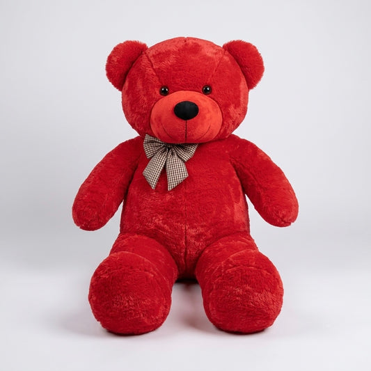 A red plush teddy bear sitting upright against a light gray studio background, with a small checkered bow around its neck.