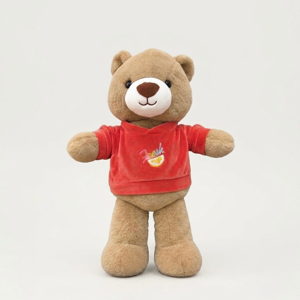 A plush brown teddy bear wearing a red short-sleeve shirt with a small colorful graphic on the chest, standing against a plain light gray background.