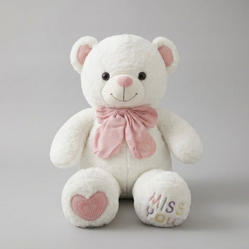 A white plush teddy bear with pink inner ears, a pink bow tie, a pink heart patch on one foot, and 'Miss You' embroidered on the other foot, set against a neutral gray background.