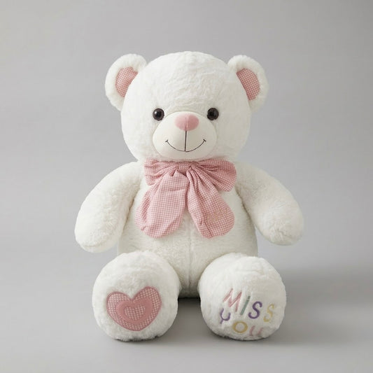 A white plush teddy bear with pink inner ears, a pink bow tie, a pink heart patch on one foot, and 'Miss You' embroidered on the other foot, set against a neutral gray background.