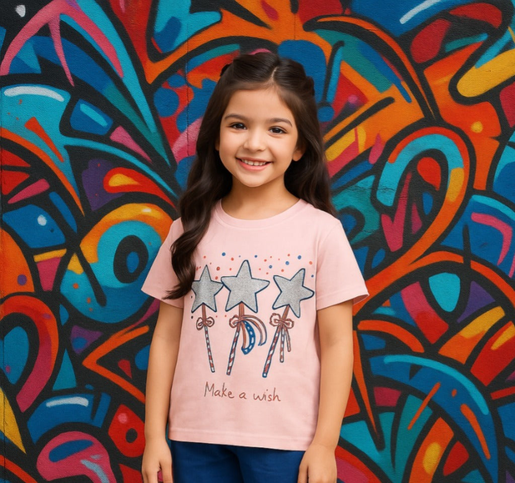 Young girl wearing a pink t-shirt with star designs and text, standing in front of a colorful abstract mural.