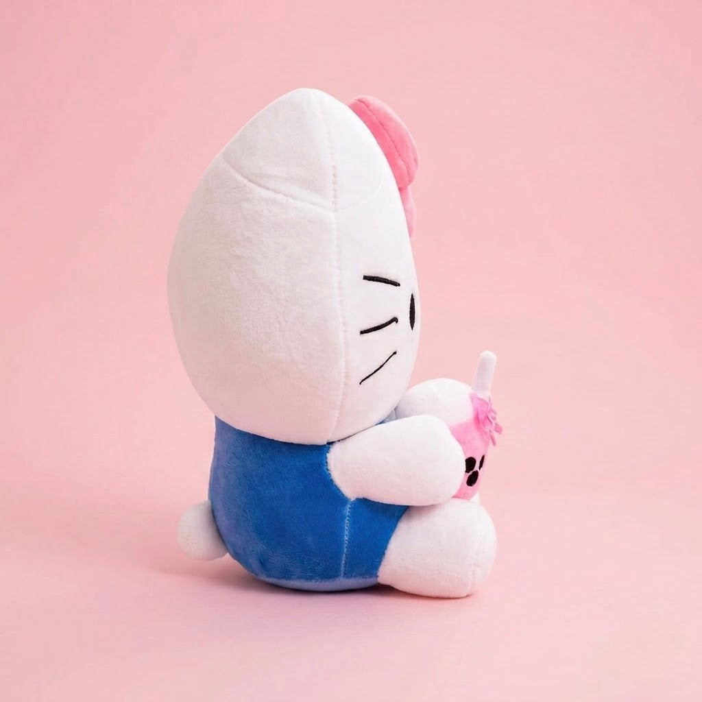 A Hello Kitty plush toy shown from the back, wearing a blue outfit and holding a small pink object, set against a solid pink background.